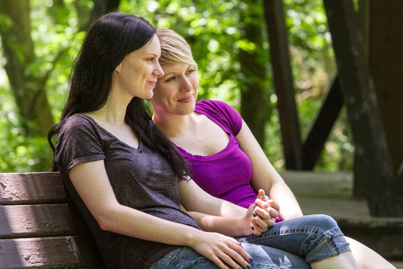 Lesbian couple holding hands and sitting on a bench in a park.