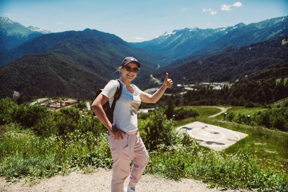 young stylish woman hiking alone with backpack enjoying beauty of mountains showing thumb up gesture